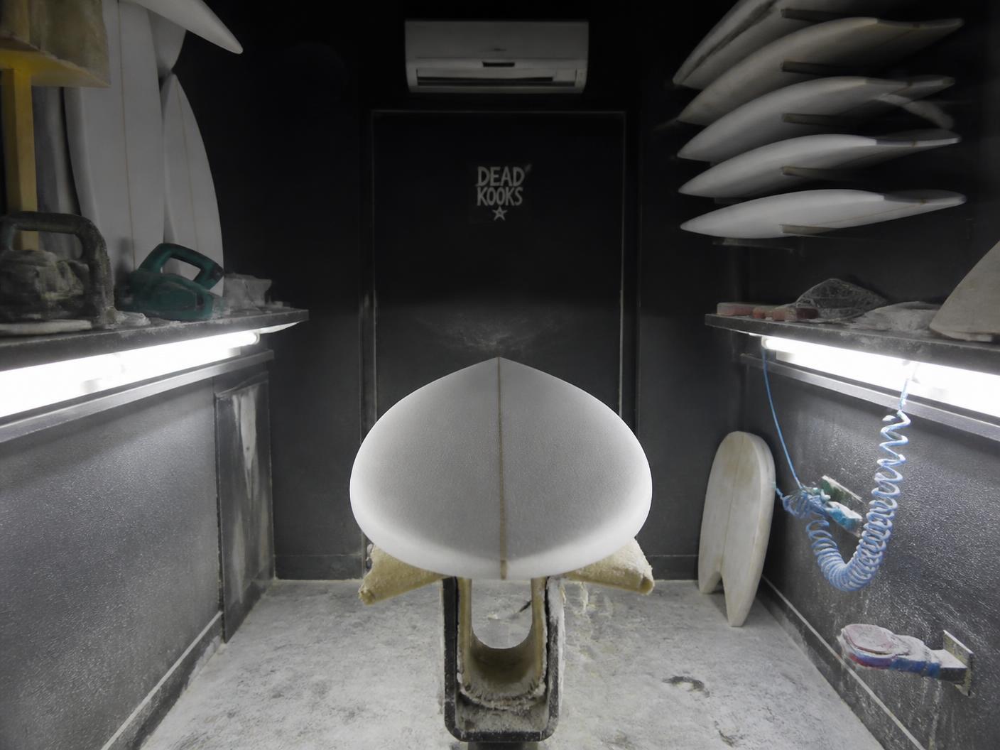 Inside the Zeebrand shaping bay with foam dust, racks of blanks and side lighting